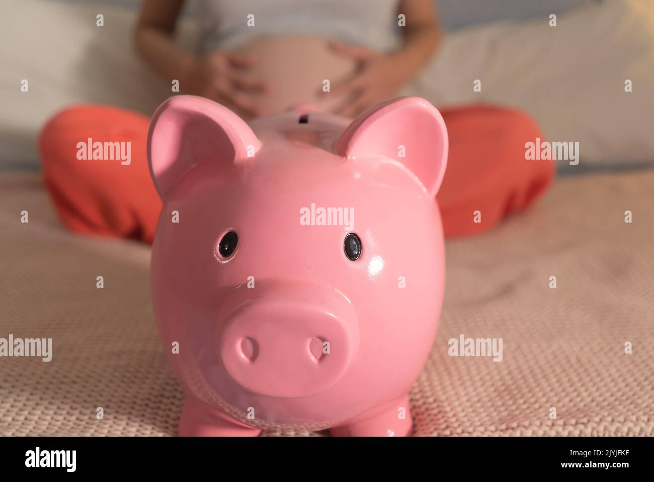 conceptual image of pink piggy bank and pregnant woman touching her belly in parenthood future expenses  and domestic finance concept Stock Photo