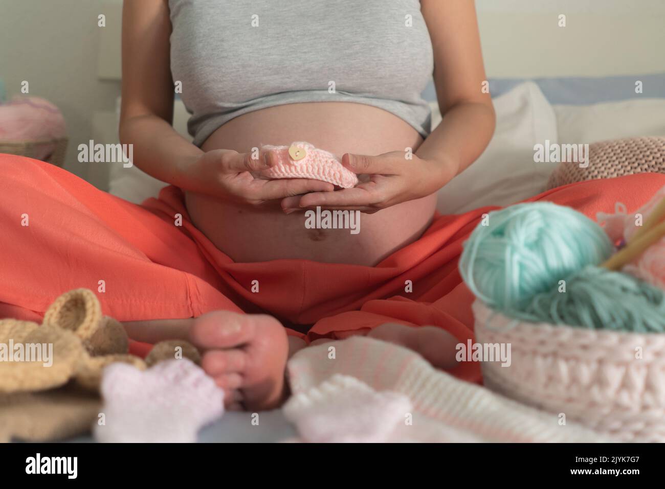 lifestyle home portrait of young happy pregnant woman holding baby boots relaxed in her bedroom in maternity and handmade knitting concept Stock Photo