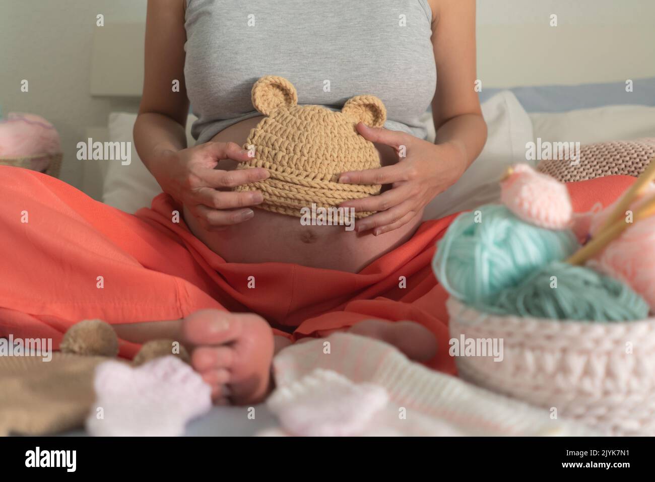 lifestyle home portrait of young happy woman knitting showing little bonnet for the new baby relaxed in her bedroom in maternity and handicraft concep Stock Photo