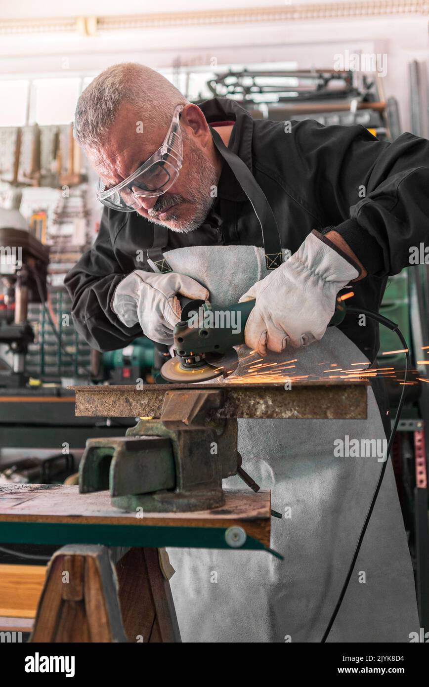 A man welder with safety glasses polishes the metal angle grinder in the workshop, sideways flashes. Male hands in gloves cut a piece of iron with spa Stock Photo