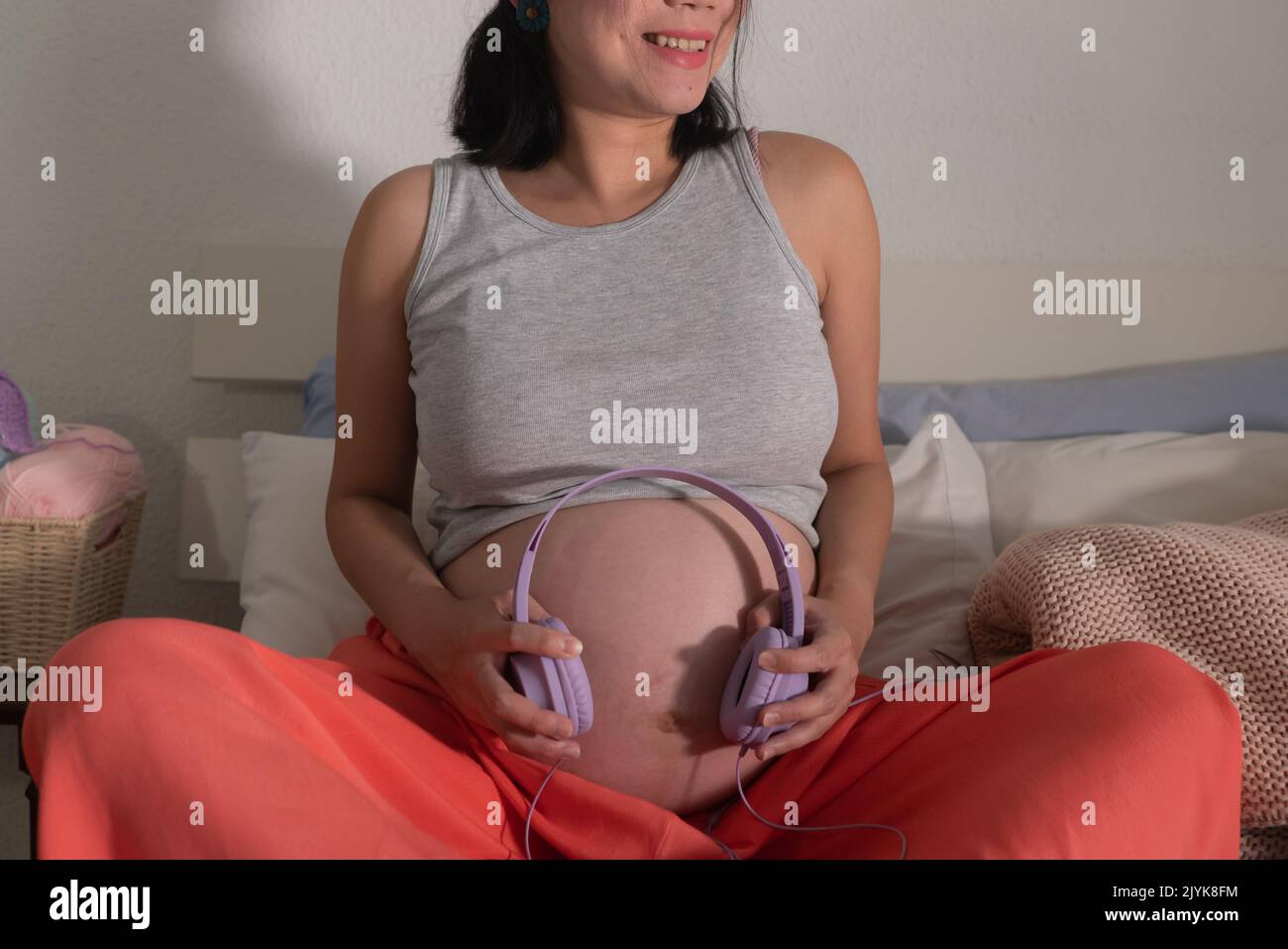 pregnancy home portrait of young happy and beautiful woman sitting pregnant on bed sharing music with her upcoming new baby putting headphones on her Stock Photo