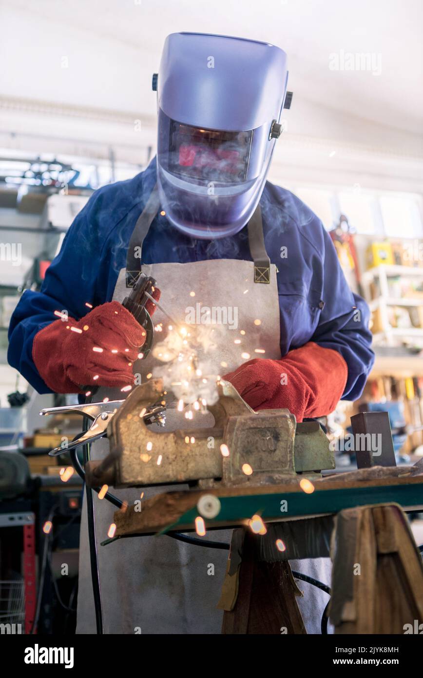 Metal processing with a man using welding machine for steel seam. Locksmith in special clothes, helmet and gloves to works in production. Sparks in me Stock Photo