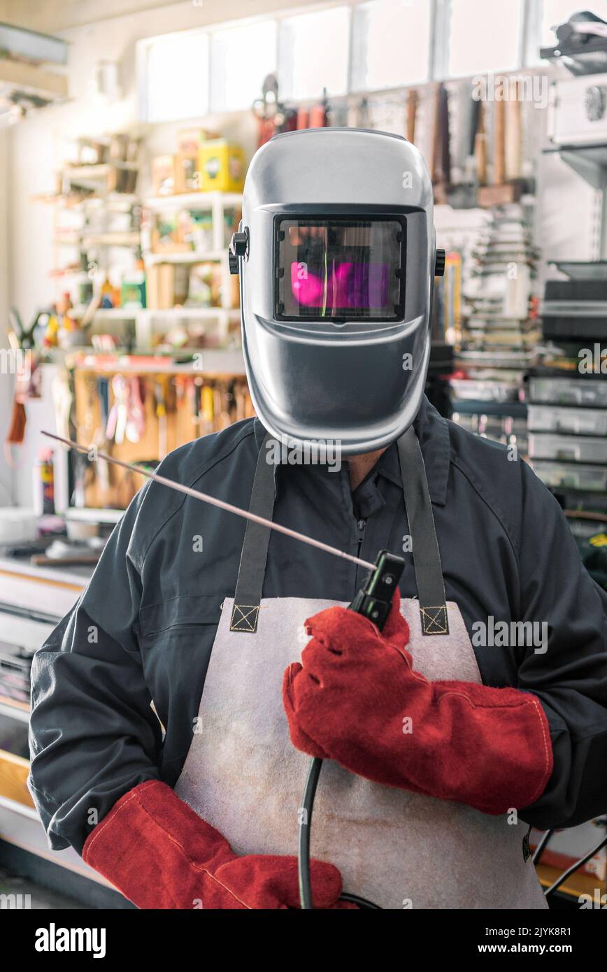 Metal processing with a man using welding machine for steel seam. Locksmith in special clothes, helmet and gloves to works in production metalworking Stock Photo