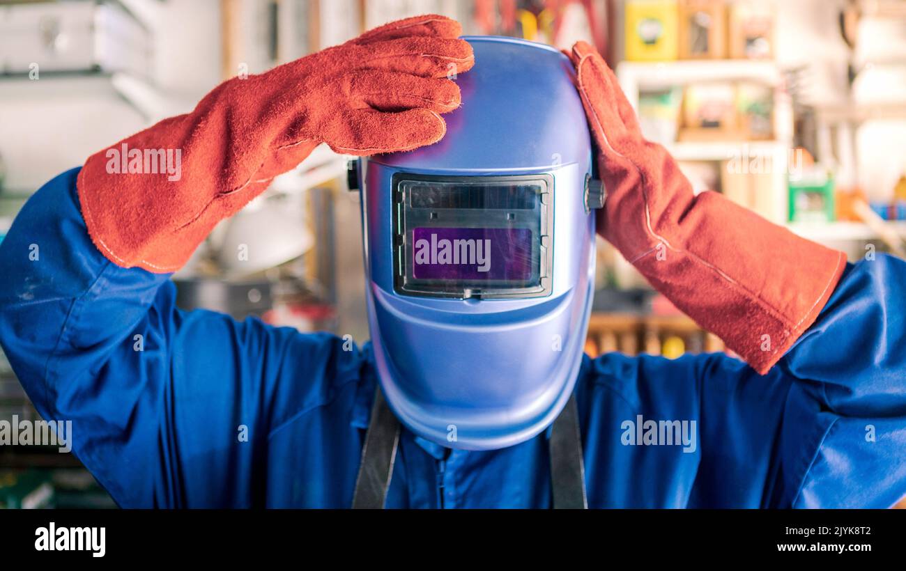 A man welder putting helmet for protect the eyes. Worker wearing a special clothes works as welding machine in his workshop, safety concept. Stock Photo