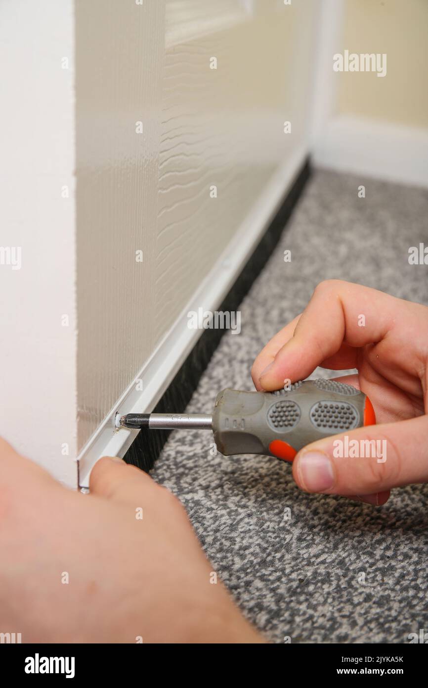 A Man fitting a draught excluder to a door in the UK to reduce heat loss and save energy. Stock Photo