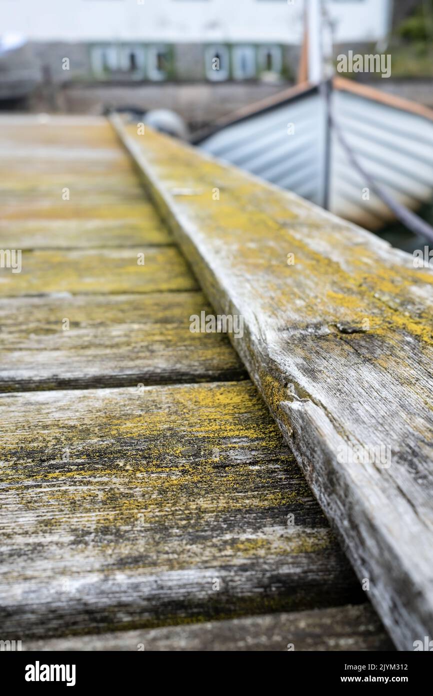 Old weathered wooden pier and a moored sailboat in the background, out of focus. Stock Photo