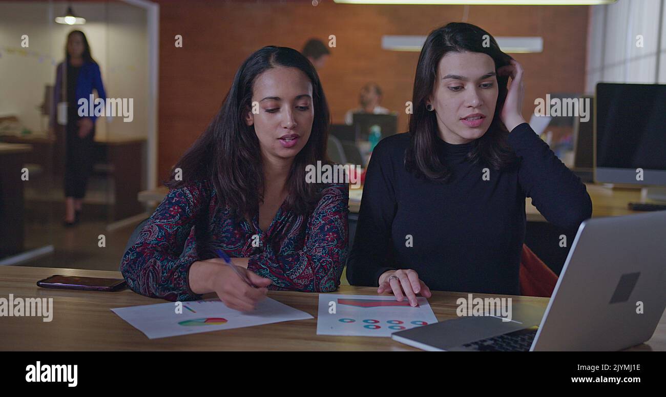 Two diverse female employees working at night in front of computer ...