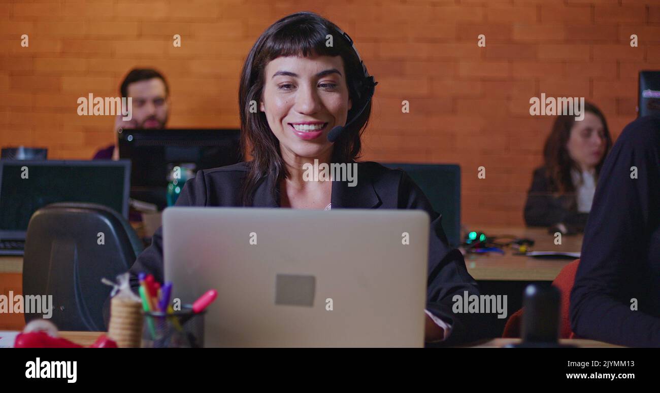 Confident young woman speaking with headset in front of computer screen ...