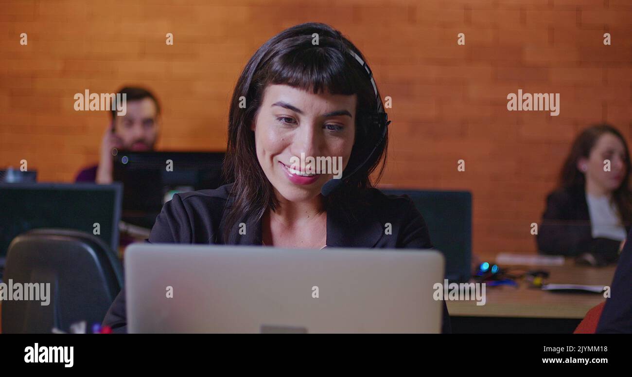 South American female employee speaking with headset in front of laptop. A hispanic latin young woman in communication via video conference speaking w Stock Photo