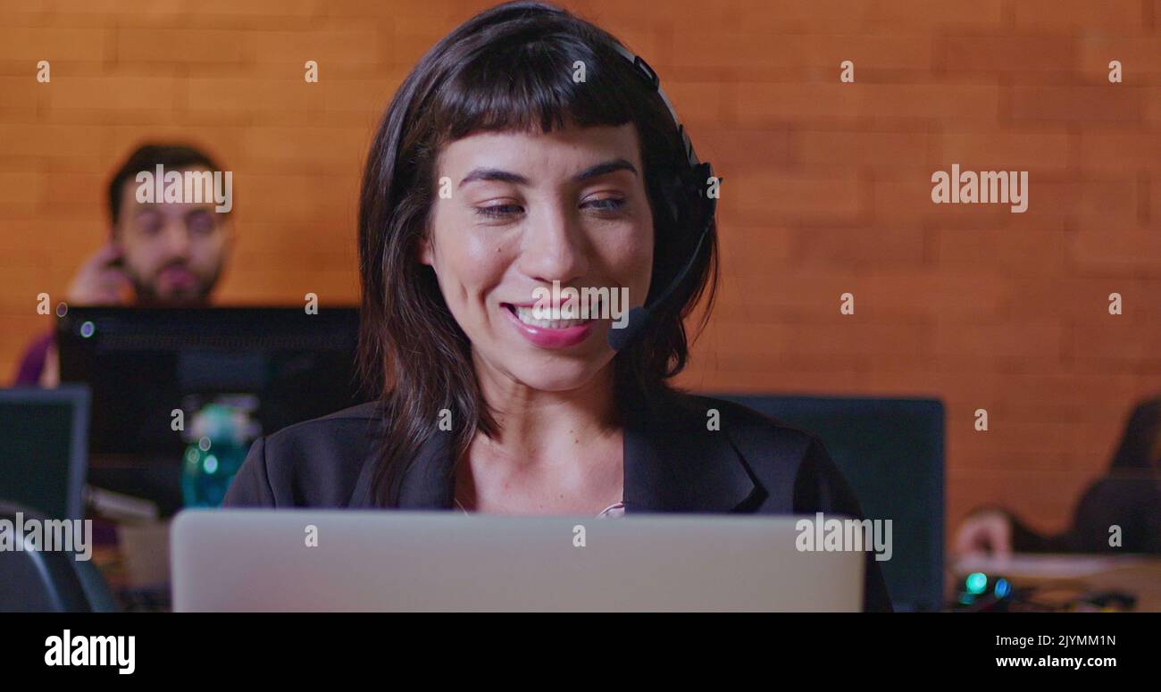 South American female employee speaking with headset in front of laptop. A hispanic latin young woman in communication via video conference speaking w Stock Photo