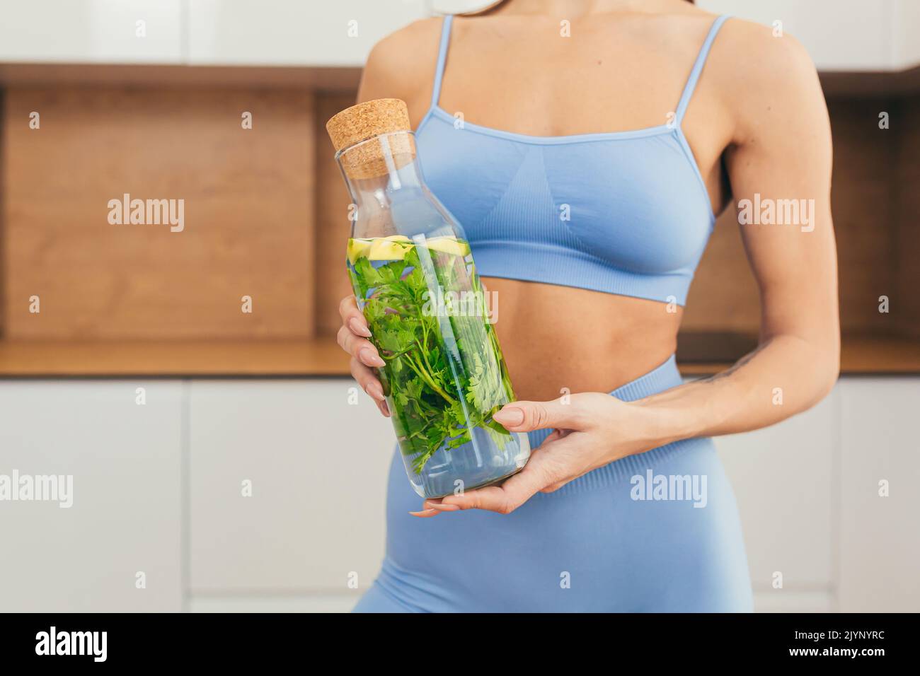 Close up photo part of body of young fitness woman holding and showing bottle of fresh juice, detox at home Stock Photo
