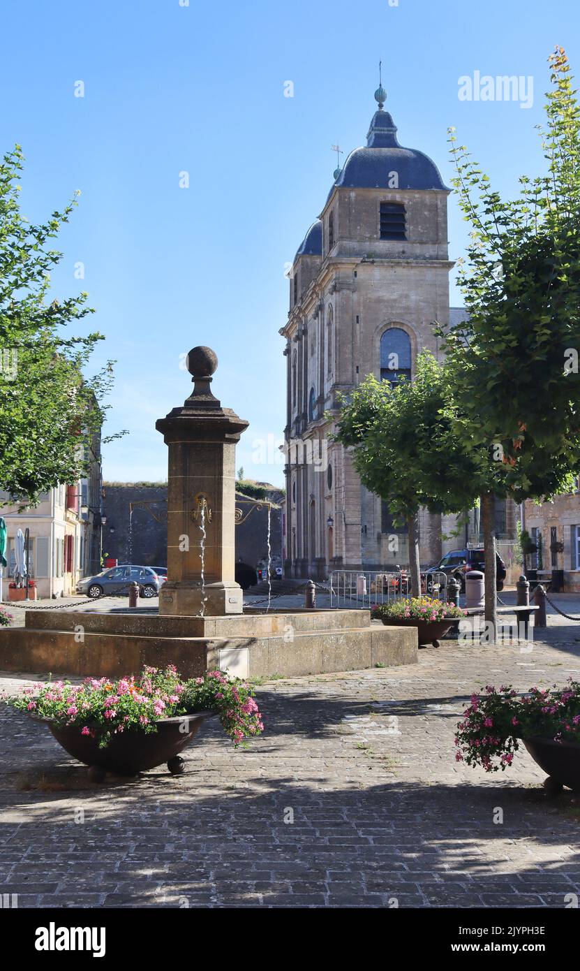 View of the main square, fountain, and church of St.Martin in Montmédy-haut, in Lorraine in France. Early on a summers morning, side lit with clear bl Stock Photo