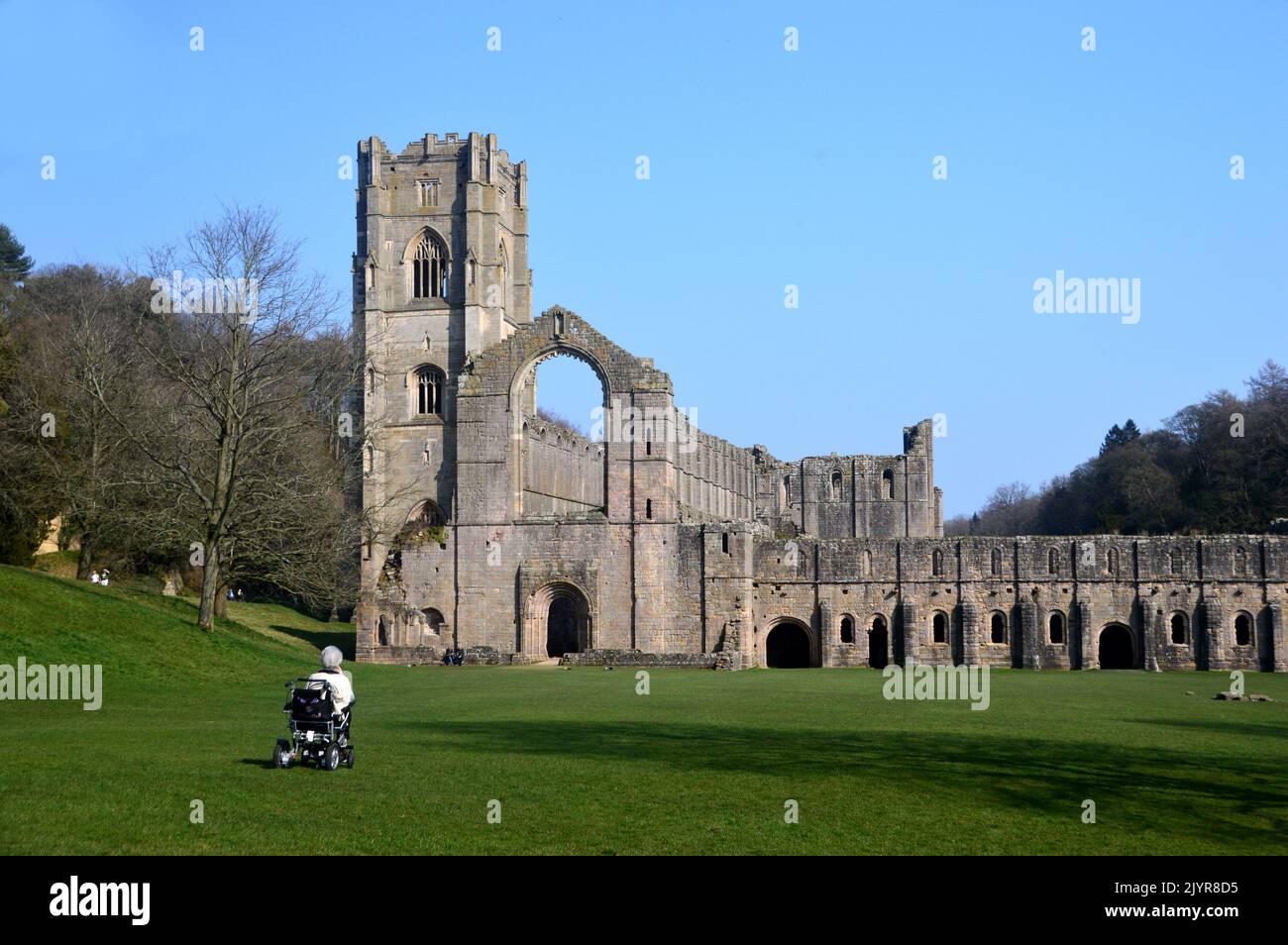 Woman in Wheelchair Looking at the Ruins of the Chapel & Bell Tower at Fountains Abbey and Studley Royal Water Garden, North Yorkshire, England, UK. Stock Photo
