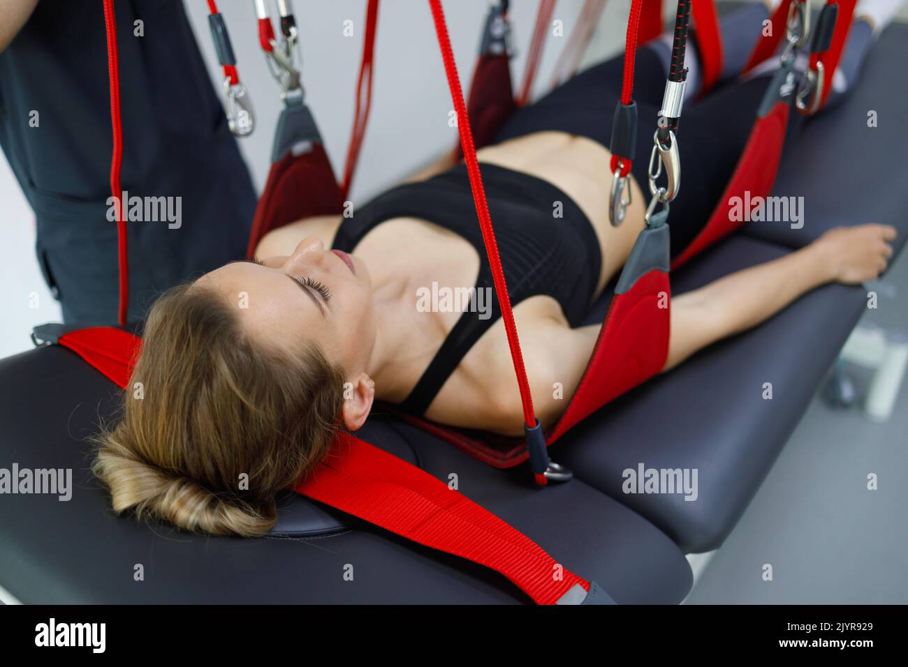 Woman hanging from red ropes during a neuromuscular activation procedure on a suspended rehabilitation system Stock Photo