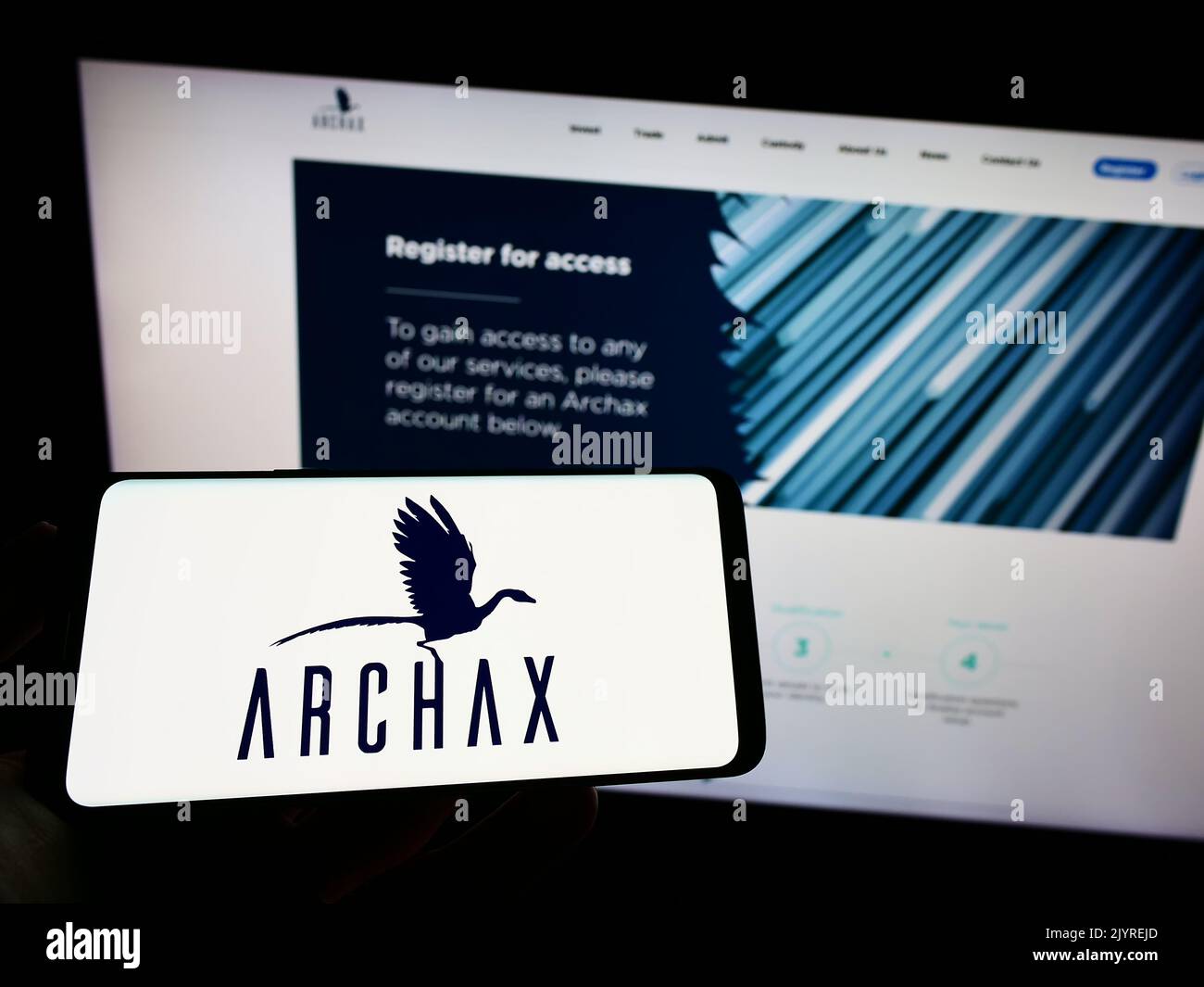 Person holding cellphone with logo of British crypto company Archax Ltd. on screen in front of business webpage. Focus on phone display. Stock Photo