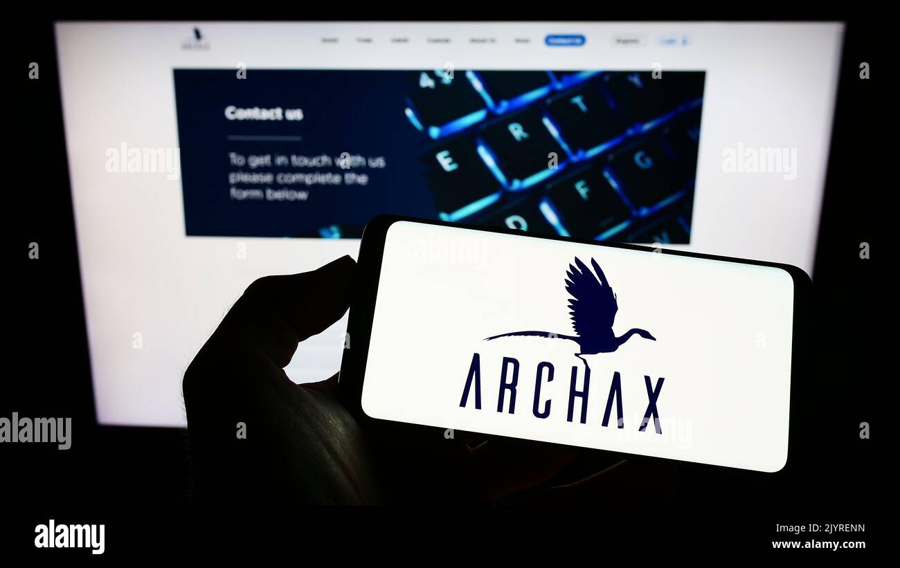 Person holding mobile phone with logo of British crypto company Archax Ltd. on screen in front of business web page. Focus on phone display. Stock Photo