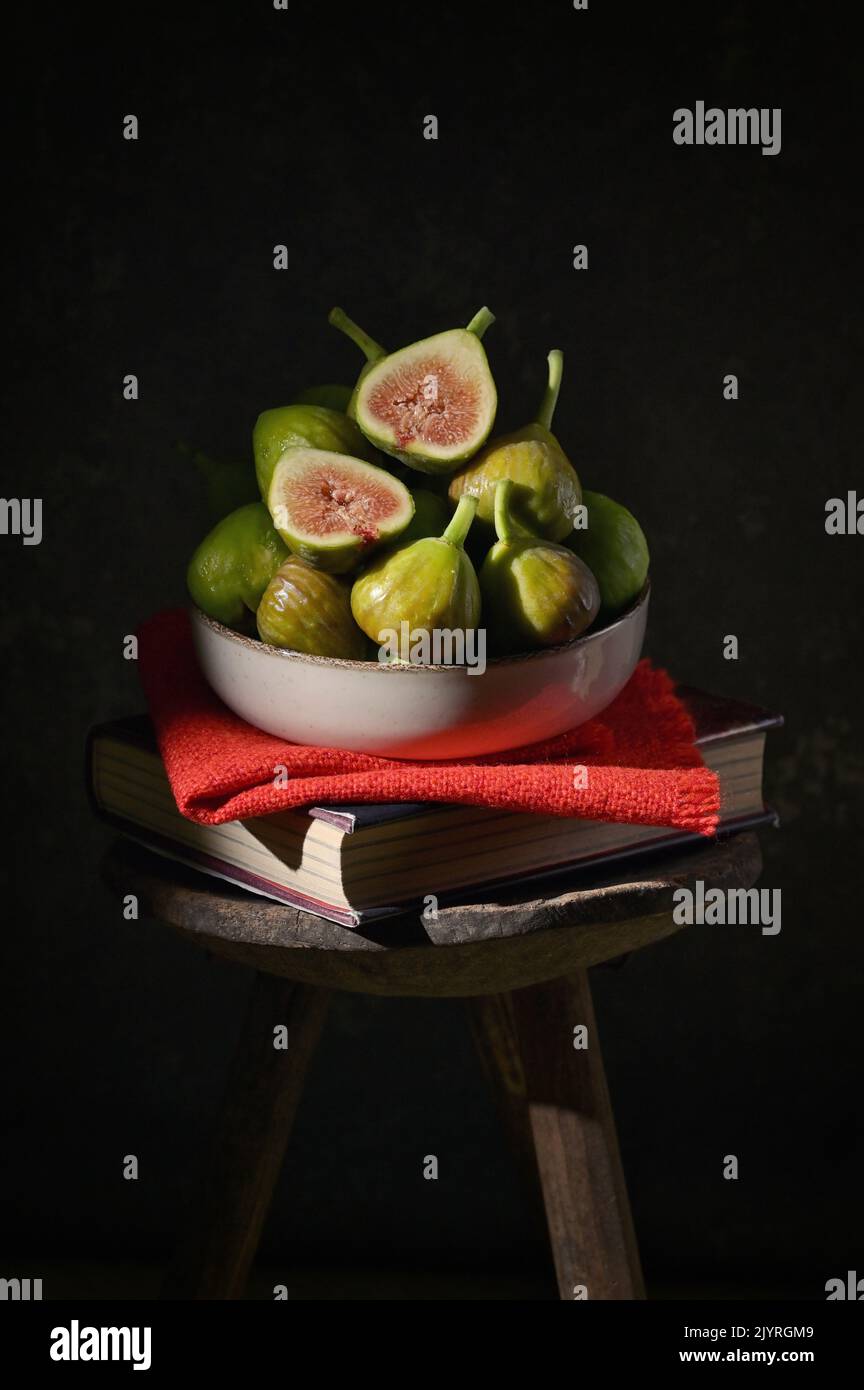 Ripe figs heap on book and old wooden stool in studio Stock Photo