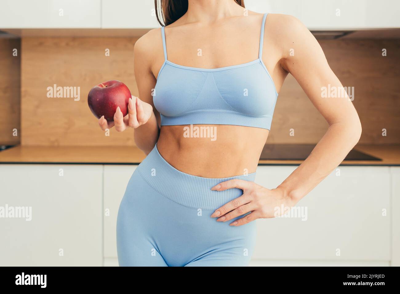 Close up photo of body part, young fitness woman holding red apple in her hand at home Stock Photo