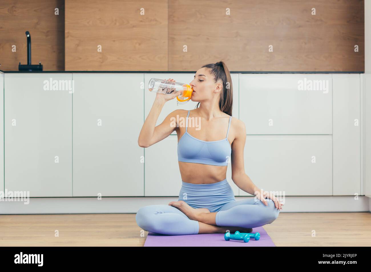 Portrait of a beautiful young fitness woman sitting on a mat in the ...