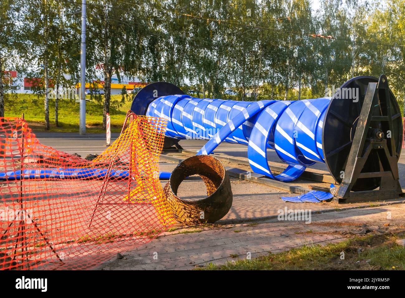 reel of U-pipe with fencing mesh on the roadway of the city when restoring an old water pipe in a trenchless way, selective focus Stock Photo