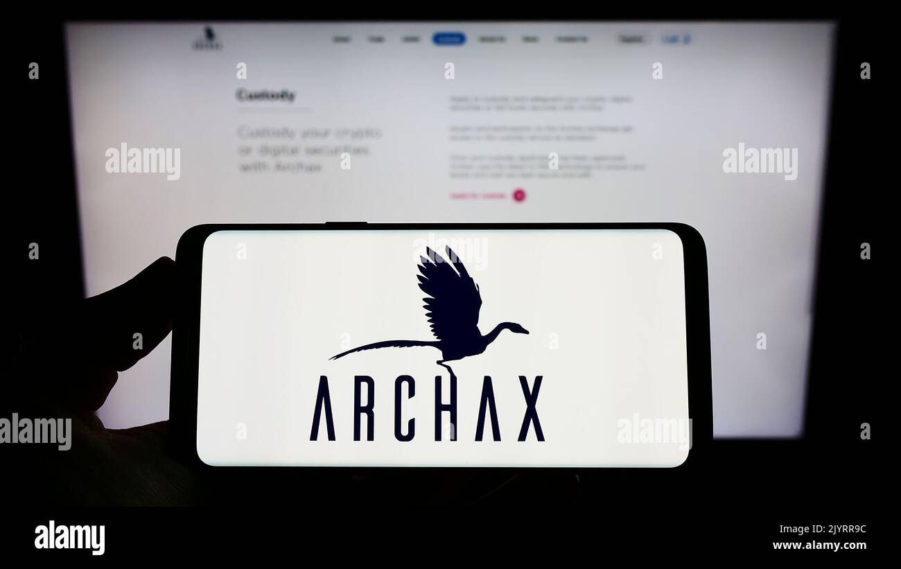 Person holding smartphone with logo of British crypto company Archax Ltd. on screen in front of website. Focus on phone display. Stock Photo