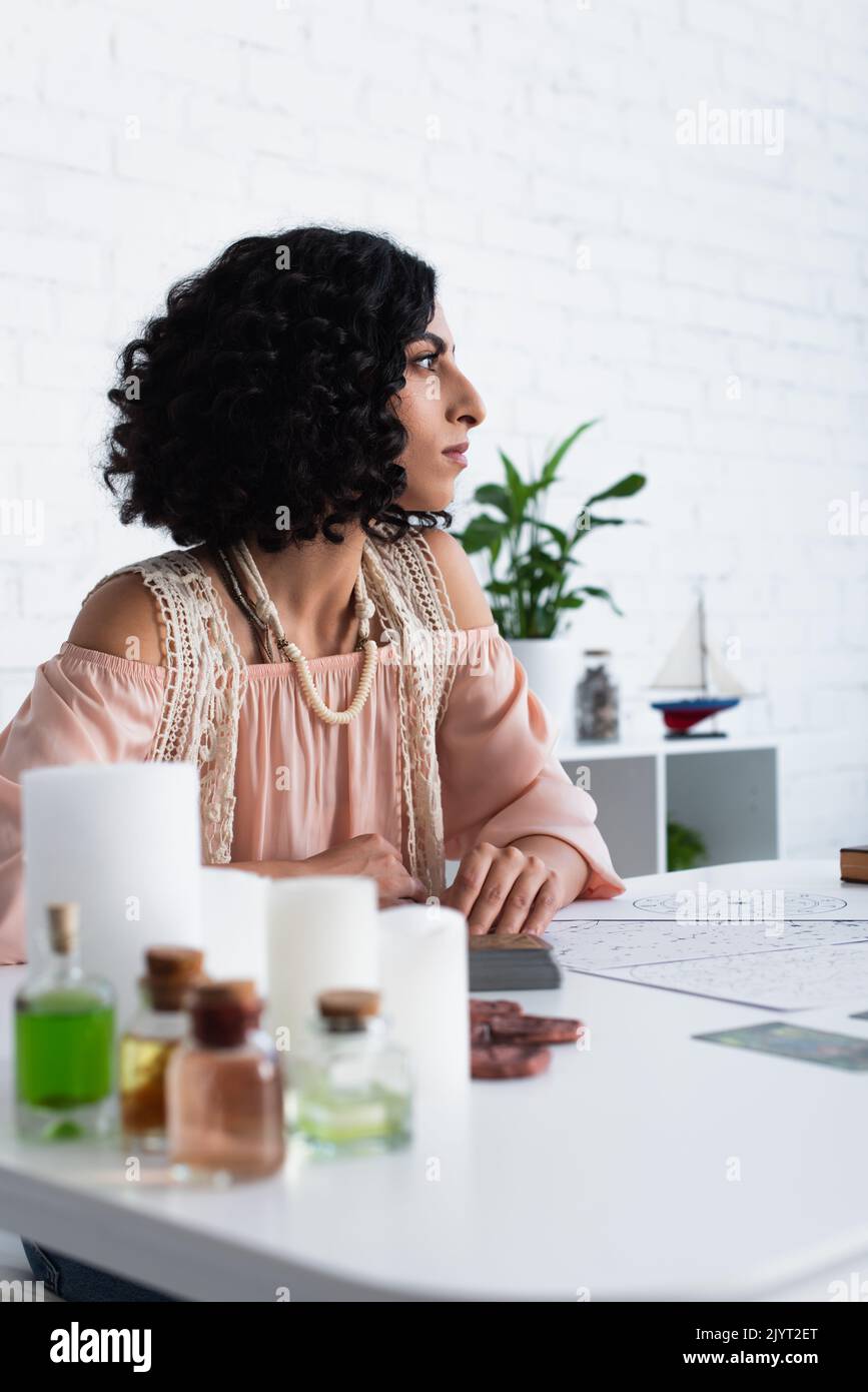 young astrologist looking away near candles and bottles with essential oils Stock Photo