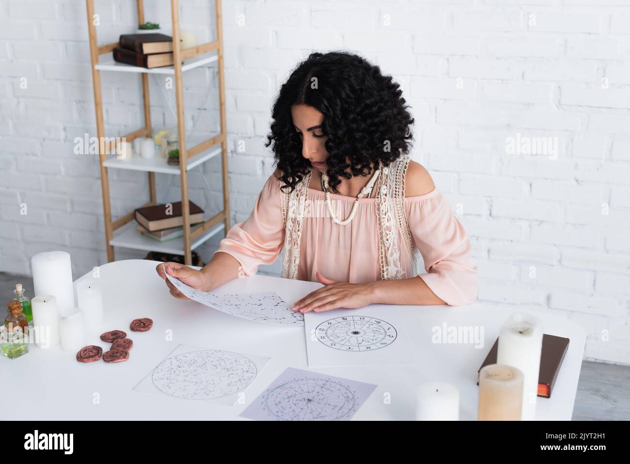 astrologer looking at constellation charts near clay runes and candles ...