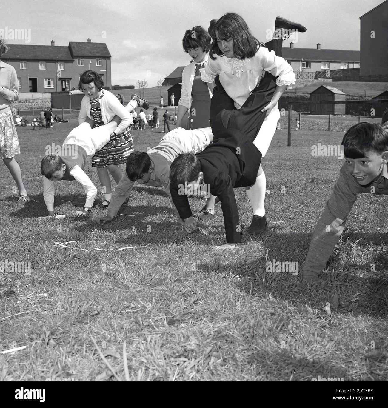 1965, historical, north queensferry gala day, youngsters taking part in a wheel-barrow race outside on the grass in a field of a housing estate at North Queensferry, Fife, Scotland, UK, the girls holding the boys legs! Stock Photo