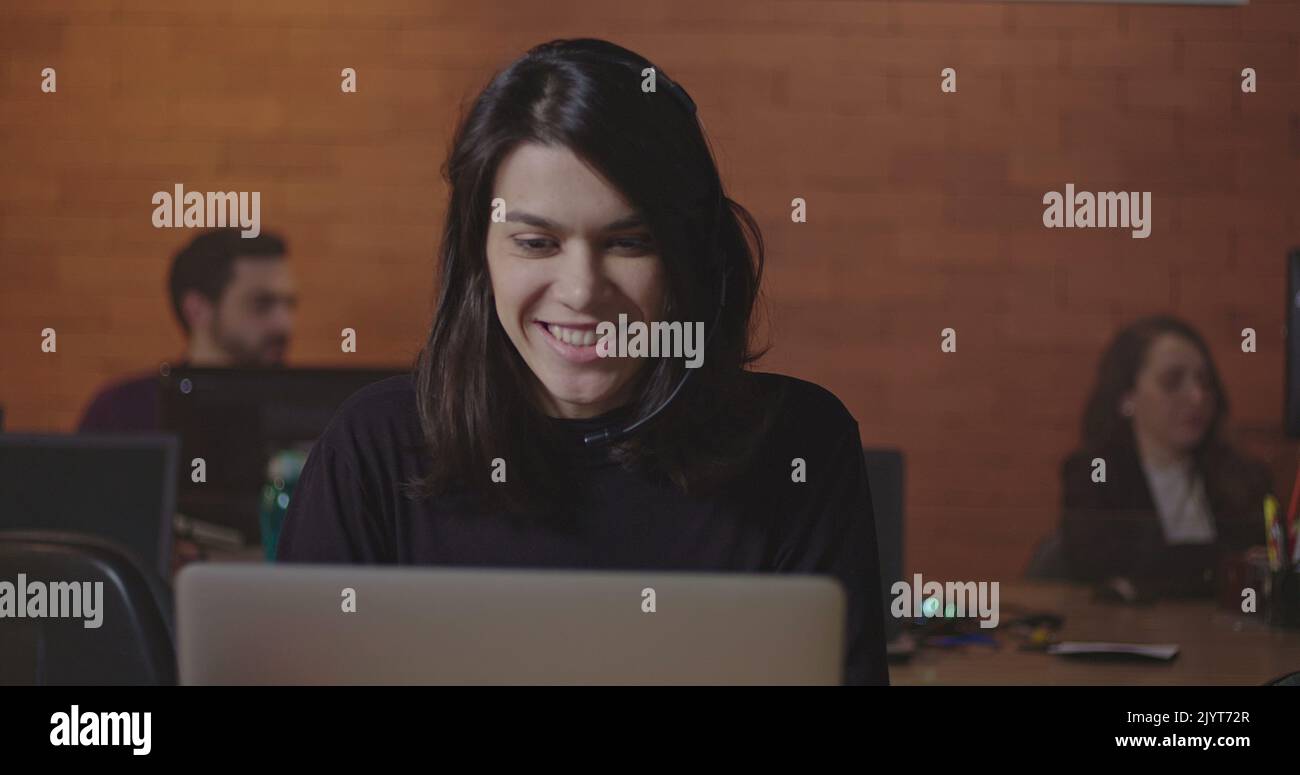 Female office employee wearing headset speaking in front of laptop ...