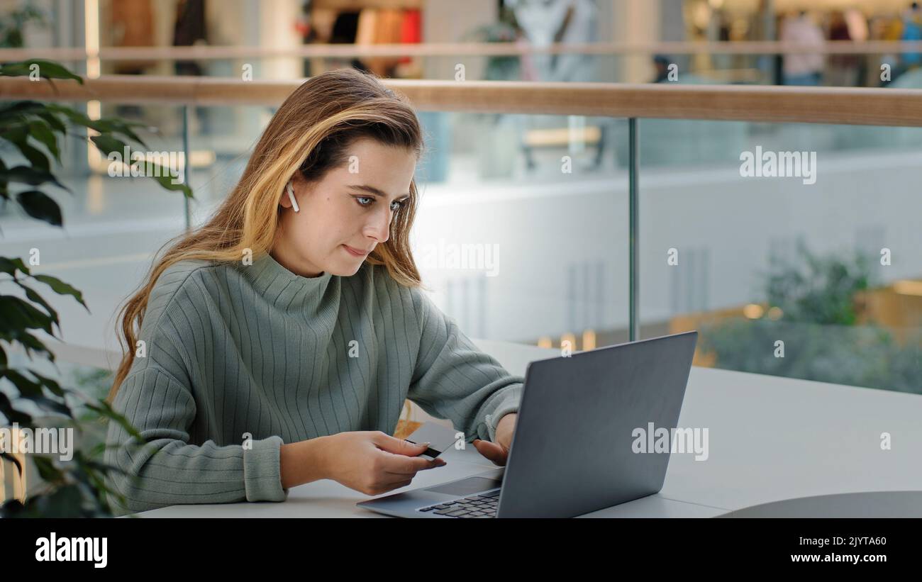 Business woman in wireless headphones girl buyer user pays website with credit card booking order online shop app using laptop computer to pay buying Stock Photo