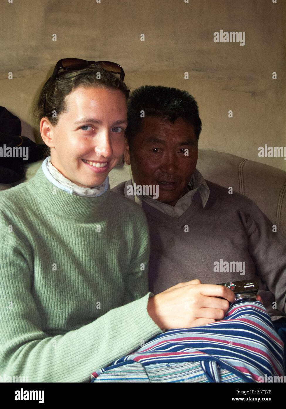 Western woman tourist shows photographs on her camera to the ethnic Tibetan family preparing cooking and eating noodle meal prepared for a visit in a small village outside Songpan ancient town in northern Sichuan province, China. PRC. (126) Stock Photo