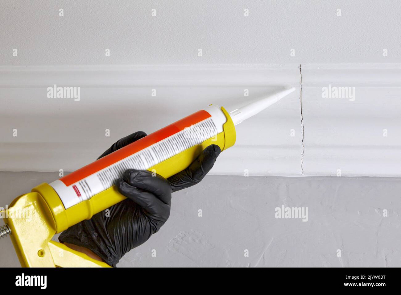 Sealing gaps in the joints of ceiling plinths. Hands in black gloves
