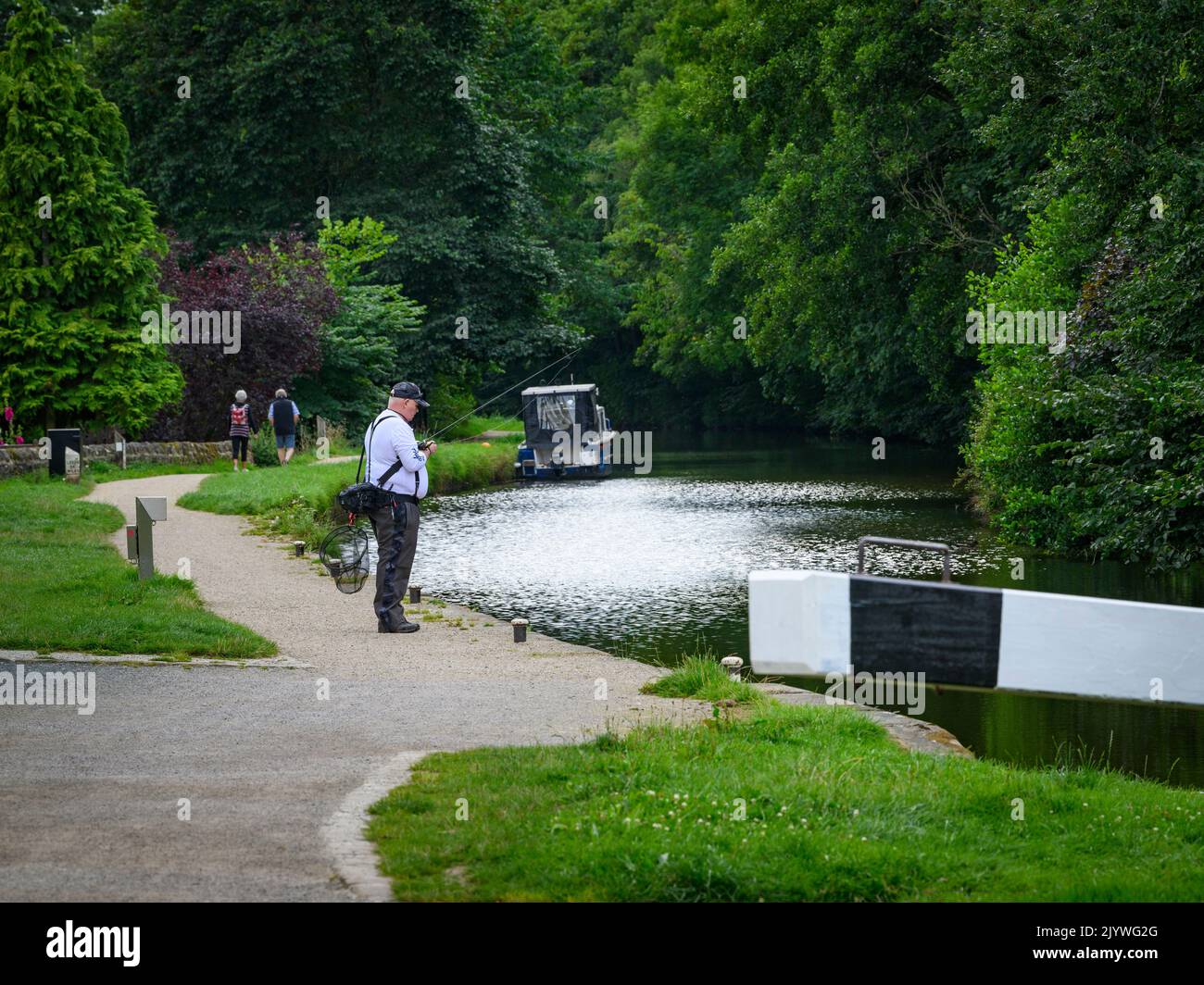 Relaxing recreational activities for people by scenic Leeds and Liverpool Canal (walkers, person angling) - Gargrave, North Yorkshire, England, UK. Stock Photo