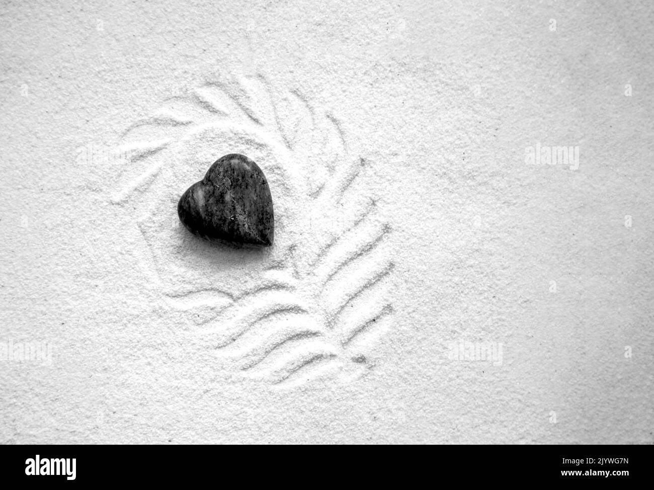 black heart stone nestled in patterned white sand. Stock Photo