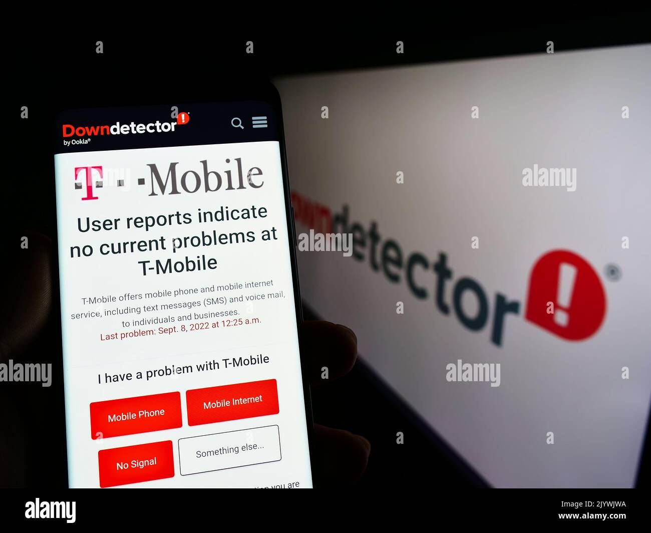 Person holding smartphone with website of platform Downdetector and T