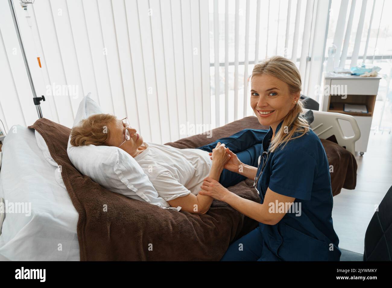 Doctor therapist holding hand of sick patient in hospital ward and looking camera Stock Photo