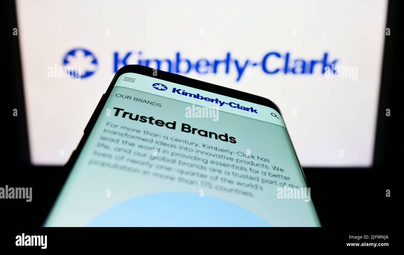 Mobile phone with website of personal care company Kimberly-Clark Corporation on screen in front of logo. Focus on top-left of phone display. Stock Photo