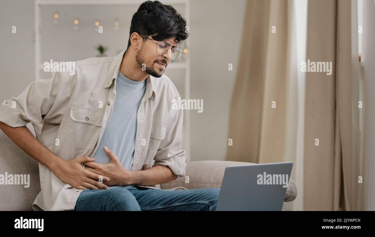 Young guy freelance business man at home working with laptop feels pain abdomen discomfort diarrhea liver problems appendicitis symptoms indigestion Stock Photo