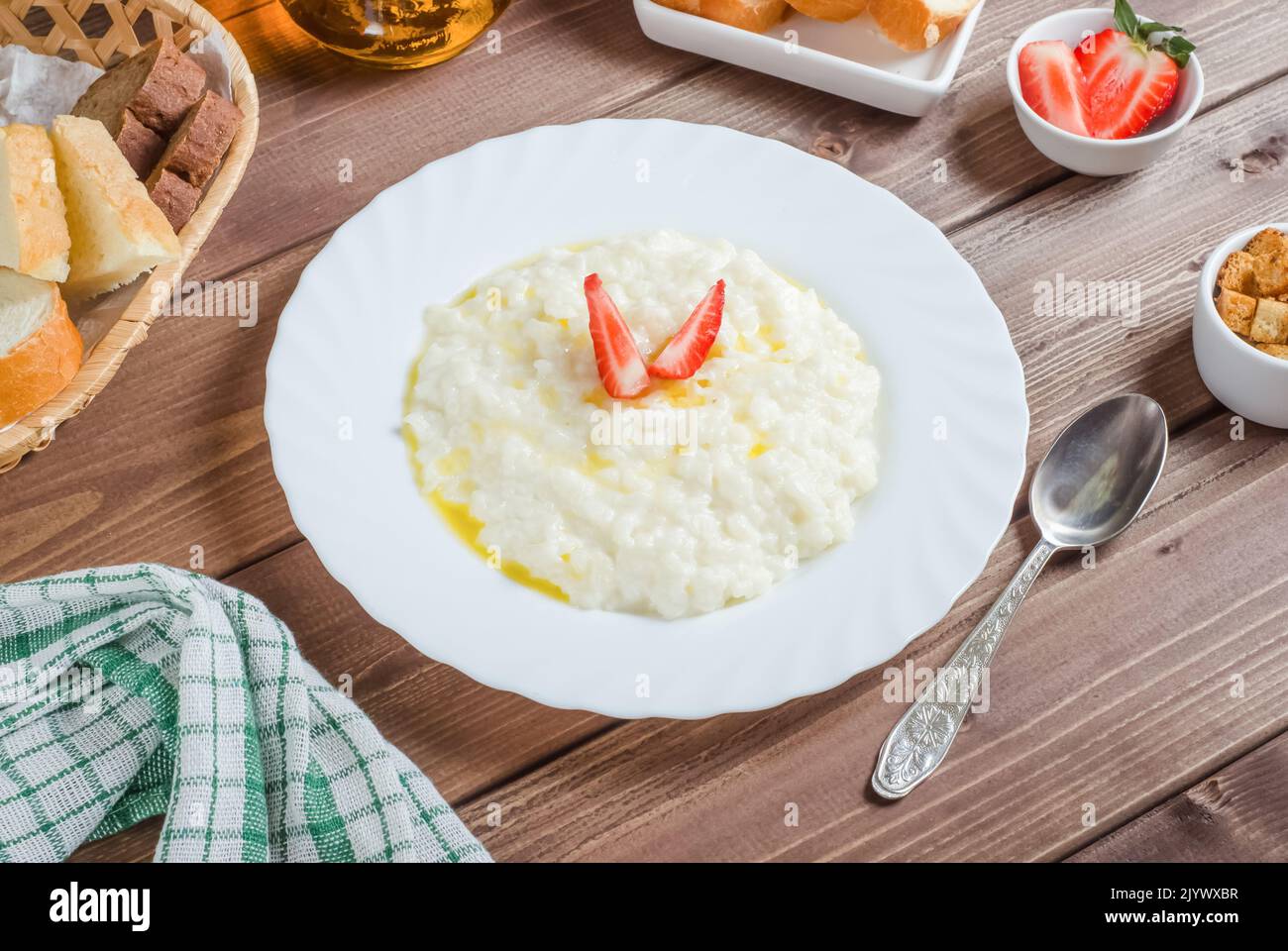 Delicious rice milk porridge with butter and strawberries in a white plate on a dark wooden background. Stock Photo