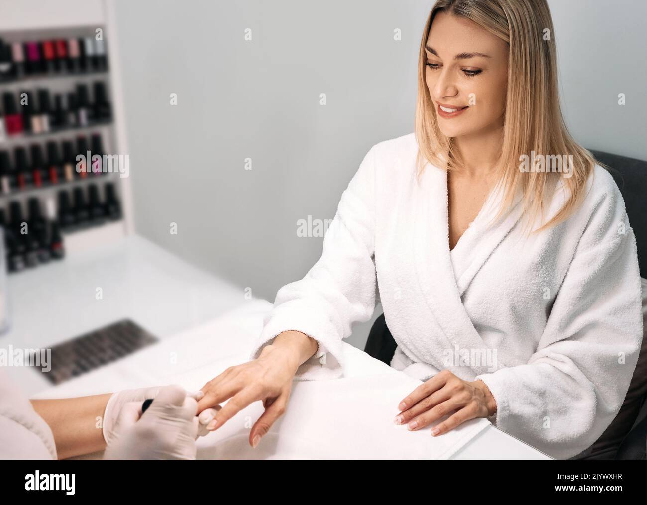 Beautiful woman in bathrobe during manicure in spa salon, taking care of her nails. Manicurist covers woman's nails with nail polish Stock Photo