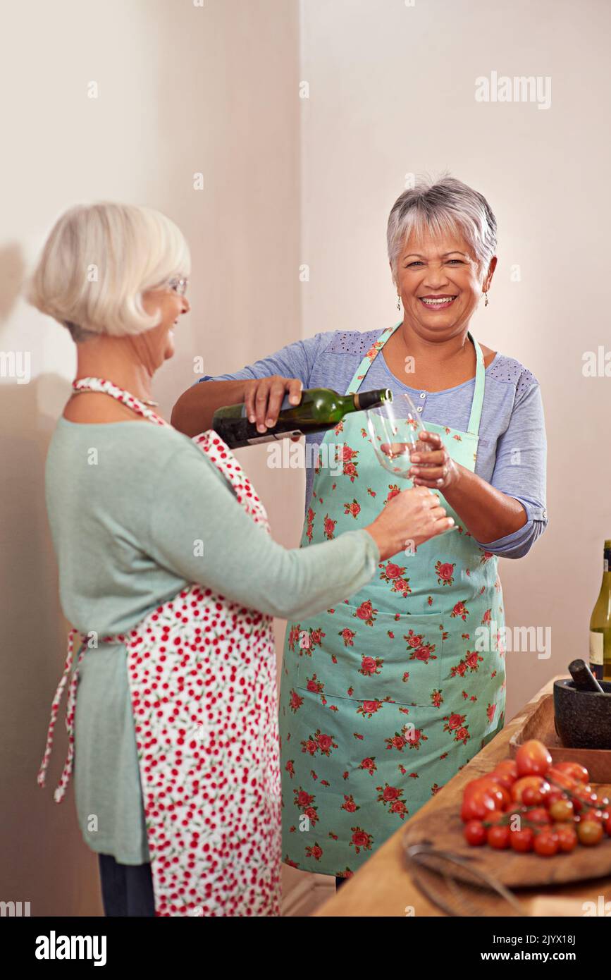 And a splash for us. two senior woman drinking wine while cooking. Stock Photo