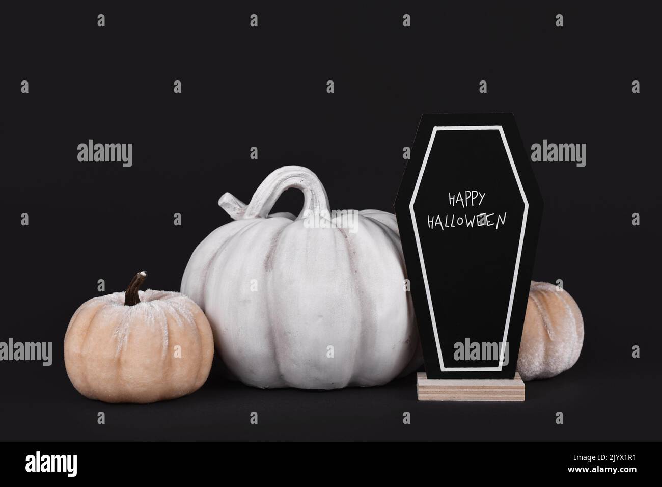 Autumn decoration with gray stone pumpkin and velvet pumpkins with coffin chalk board with text 'Happy Halloween' on black background Stock Photo