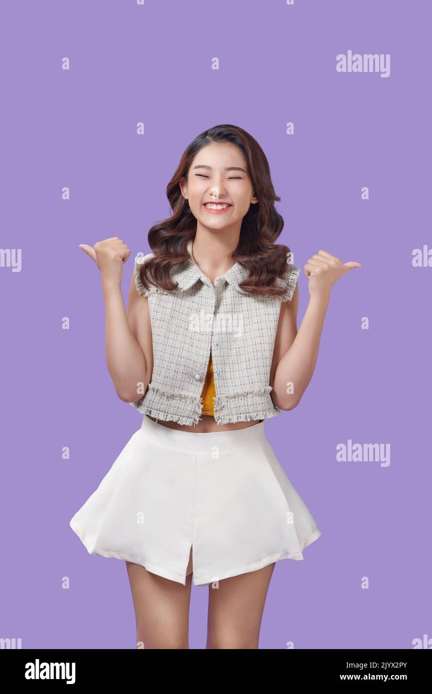 Showing and Pointing Two Product With Thumbs Of Beautiful Asian Woman Isolated On purple Background Stock Photo