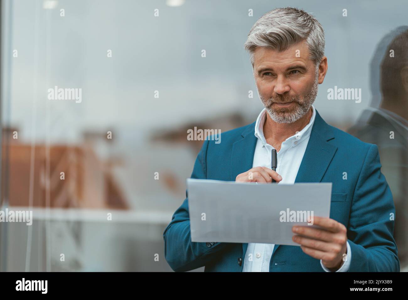 Smiling mature businessman standing outside of office with documents Stock Photo