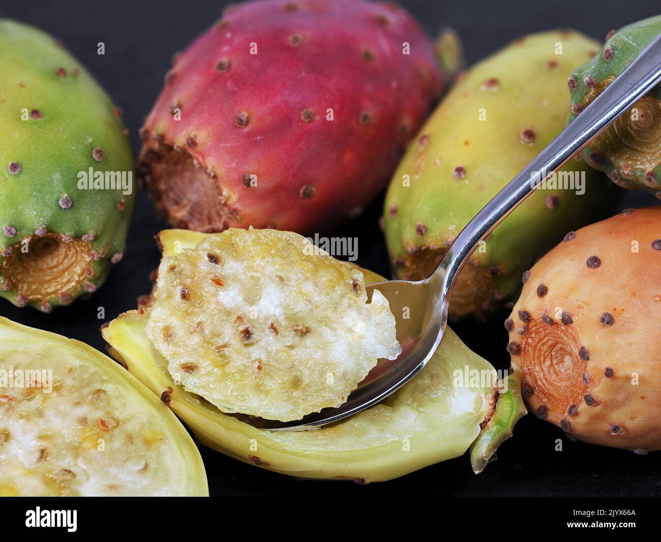 close up of a halved prickly pear cactus fig, opuntia fruit with spoon on black background Stock Photo