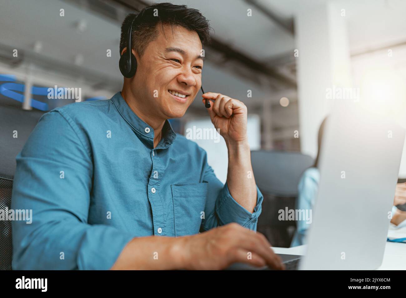 Smiling asian businessman in headphones talking online with client sitting in office Stock Photo