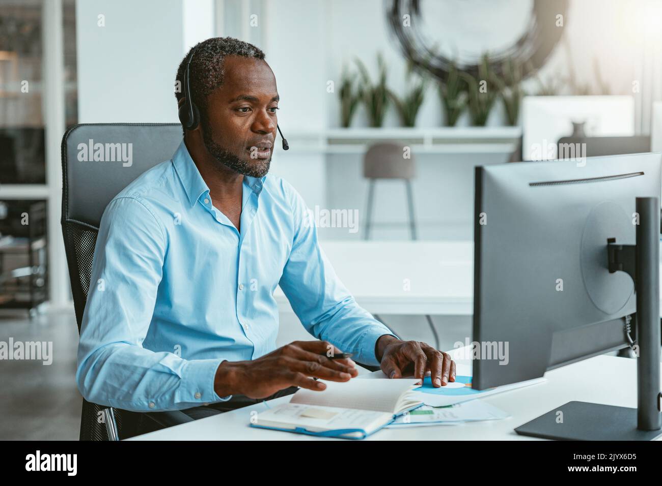 Confident African businessman taking notes and working laptop while ...