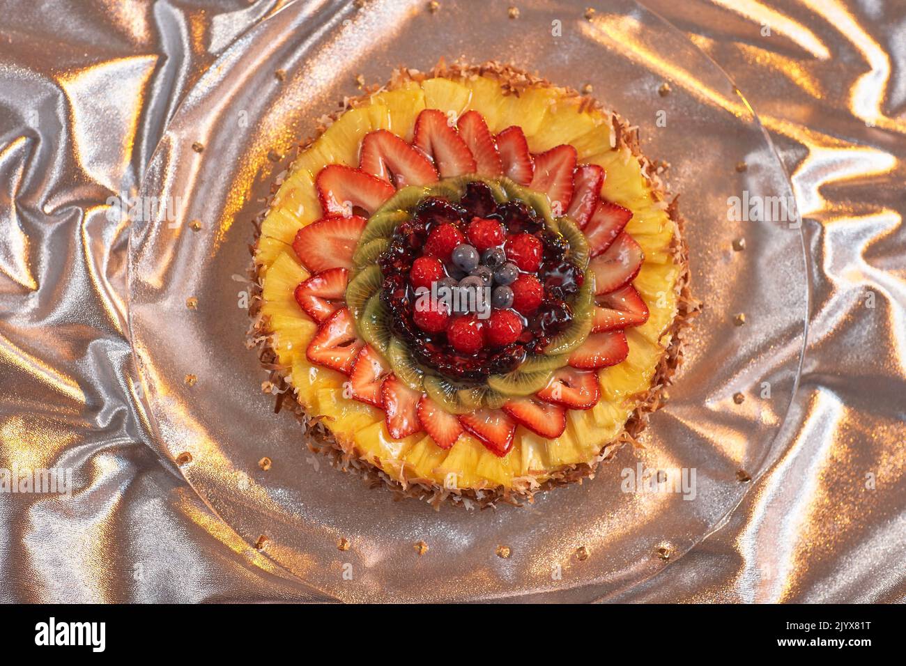 Fruit pie, round fruit pastry with toasted coconut crust.  Coconut cream custard topped with pineapple, strawberries, kiwi, blackberries, raspberries. Stock Photo