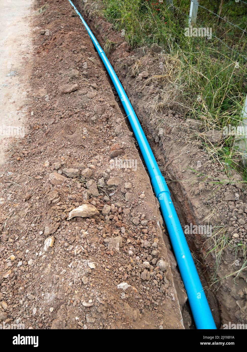 The new PVC pipe is laying in the trench along the concrete road for