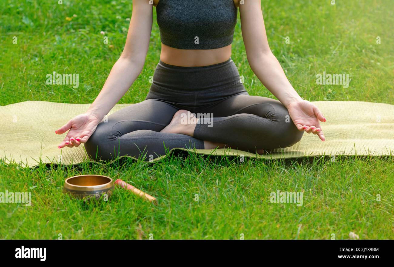 A slender woman sitting on the green grass in summer, meditates Stock Photo